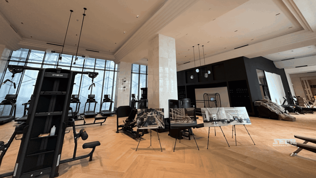 Commercial gym interior with floor-to-ceiling windows, treadmills and strength machines, and project photo boards on easels; Seer Mechanical photo.
