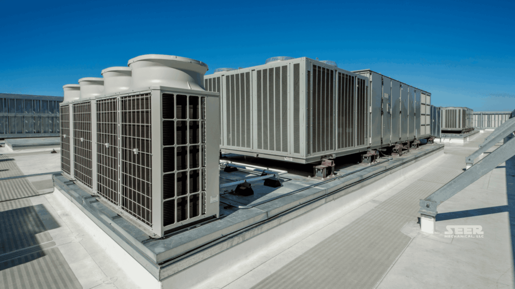 Commercial rooftop HVAC units (RTUs) on a flat building roof under a clear blue sky.