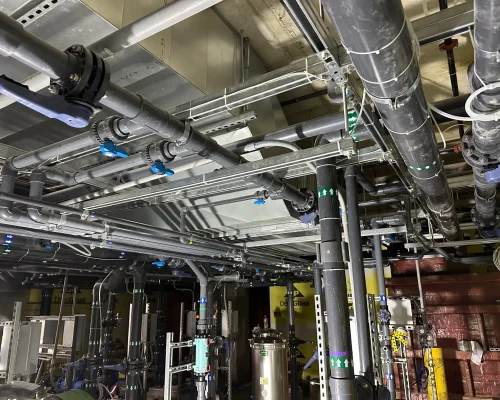 Commercial HVAC mechanical room with neatly installed overhead piping, isolation valves, and equipment racks.
